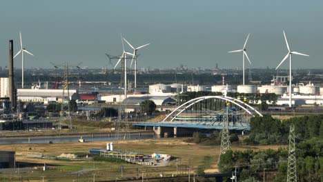 aerial wide shot of industrial buildings with port of rotterdam and rotating wind turbine during sunlight - rotterdam, netherlands