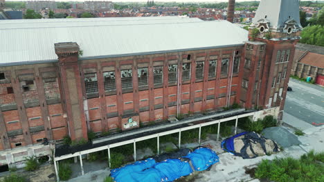 downward dolly aerial of old abandoned building with blue construction tarps in ghent