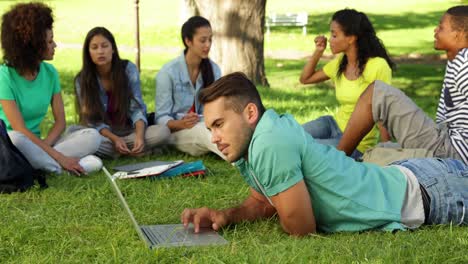 smiling student using his laptop in front of his friends