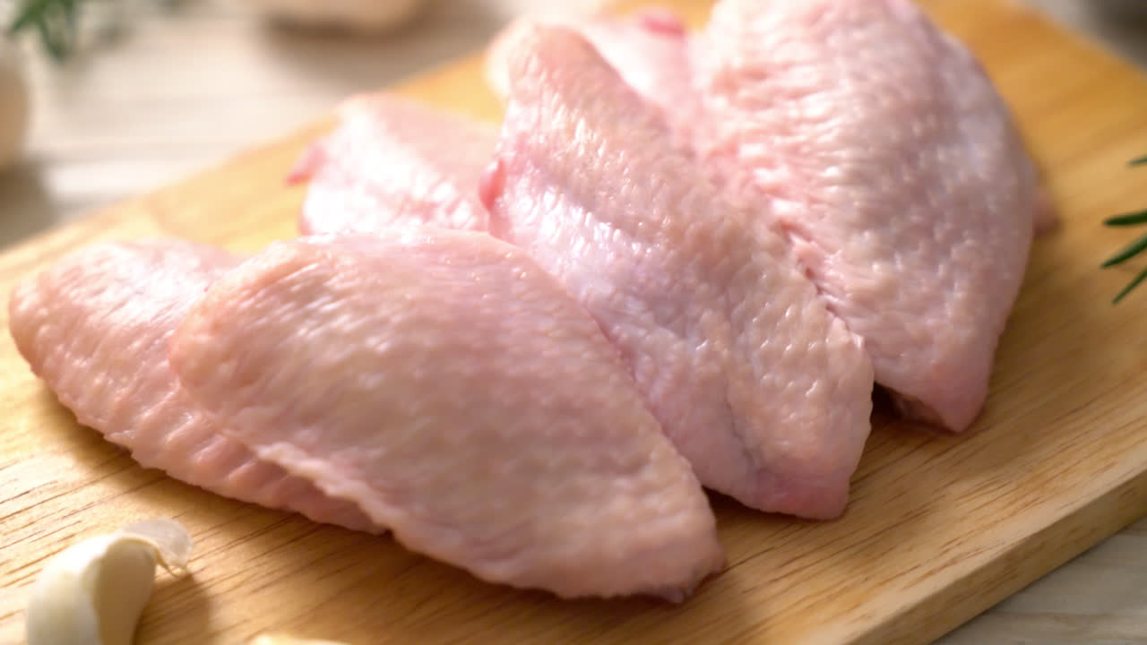 Alas de pollo medio crudo fresco sobre tabla de madera con ingredientes