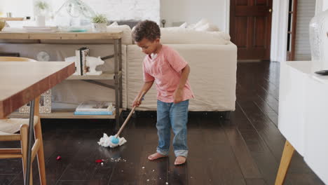 three year old african american boy cleaning dining room floor with a mop, full length