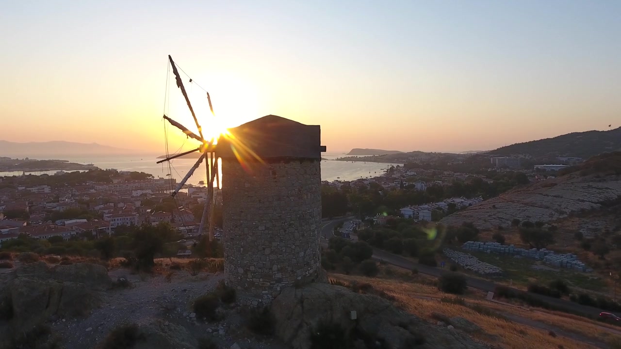 Vista Aérea de Moinho de Pedra Histórico ao Pôr do Sol com Vista para uma Cidade Costeira