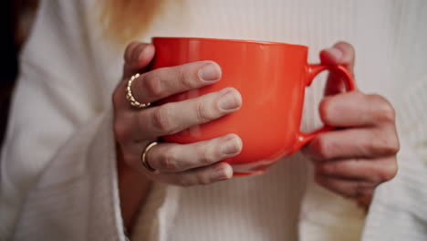 closeup of woman hands holding a big orange mug of coffee