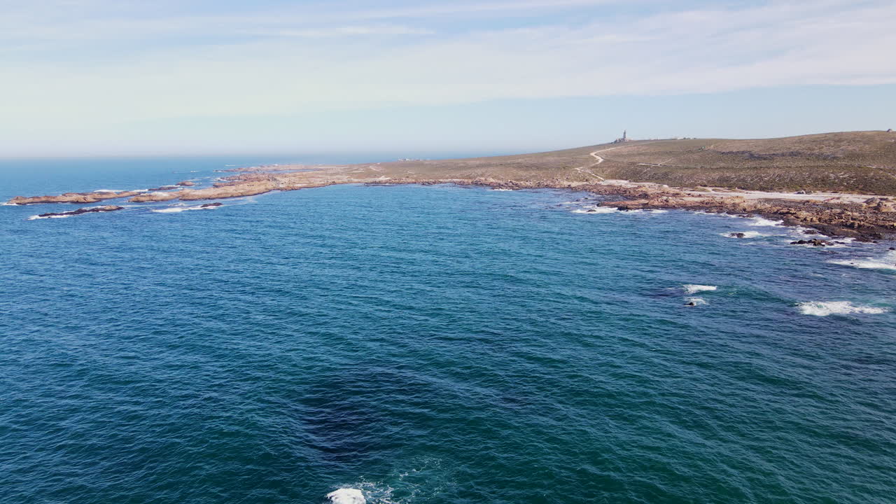 Aerial over ocean of rugged west coast shoreline and Cape Columbine lighthouse