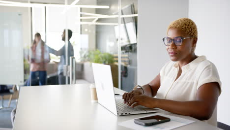 working on laptop, woman smiling at camera in modern office environment