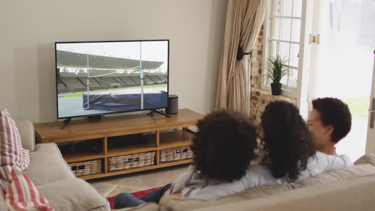 Famiglia felice seduta a casa insieme che guarda l'atletica salto in alto in TV