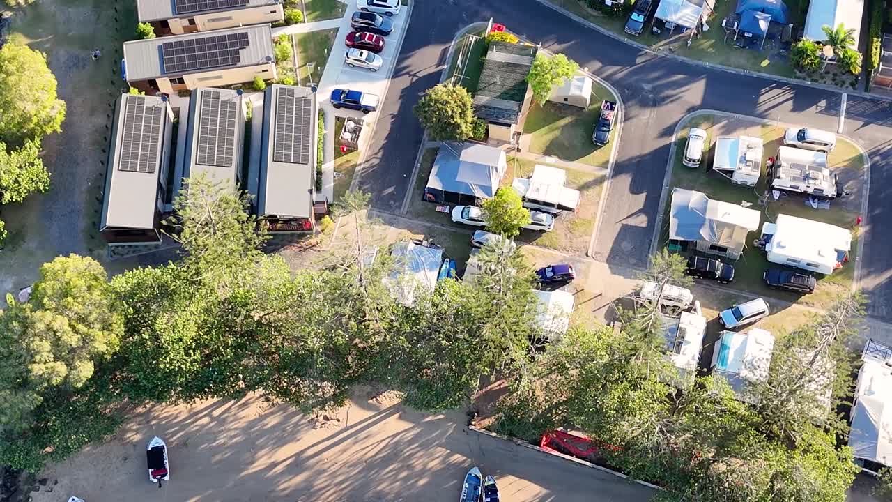 Aerial footage showcasing a caravan park by the river with moored boats and lush greenery.