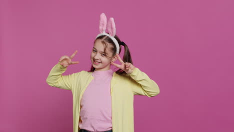 young cheerful kid with pigtails showing peace sign in studio