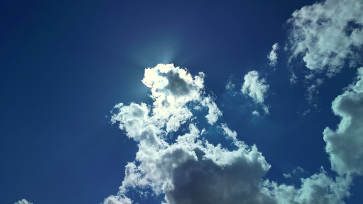Bright midday sun hides behind large white full fluffy clouds