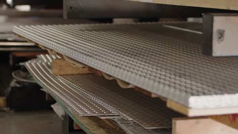primer plano de láminas metálicas apiladas con perforaciones en un taller, profundidad de campo poco profunda
