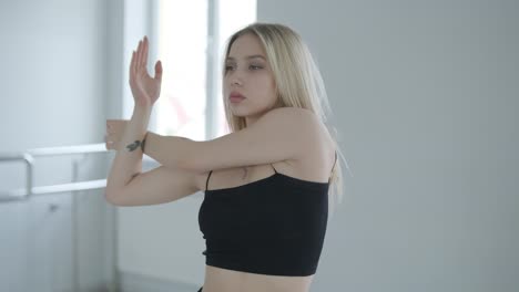 fit girl in black clothes performing contemporary. female dancer shows flowing motions, body and hands waves at white room. modern ballet dance choreography. young woman is moving smoothly