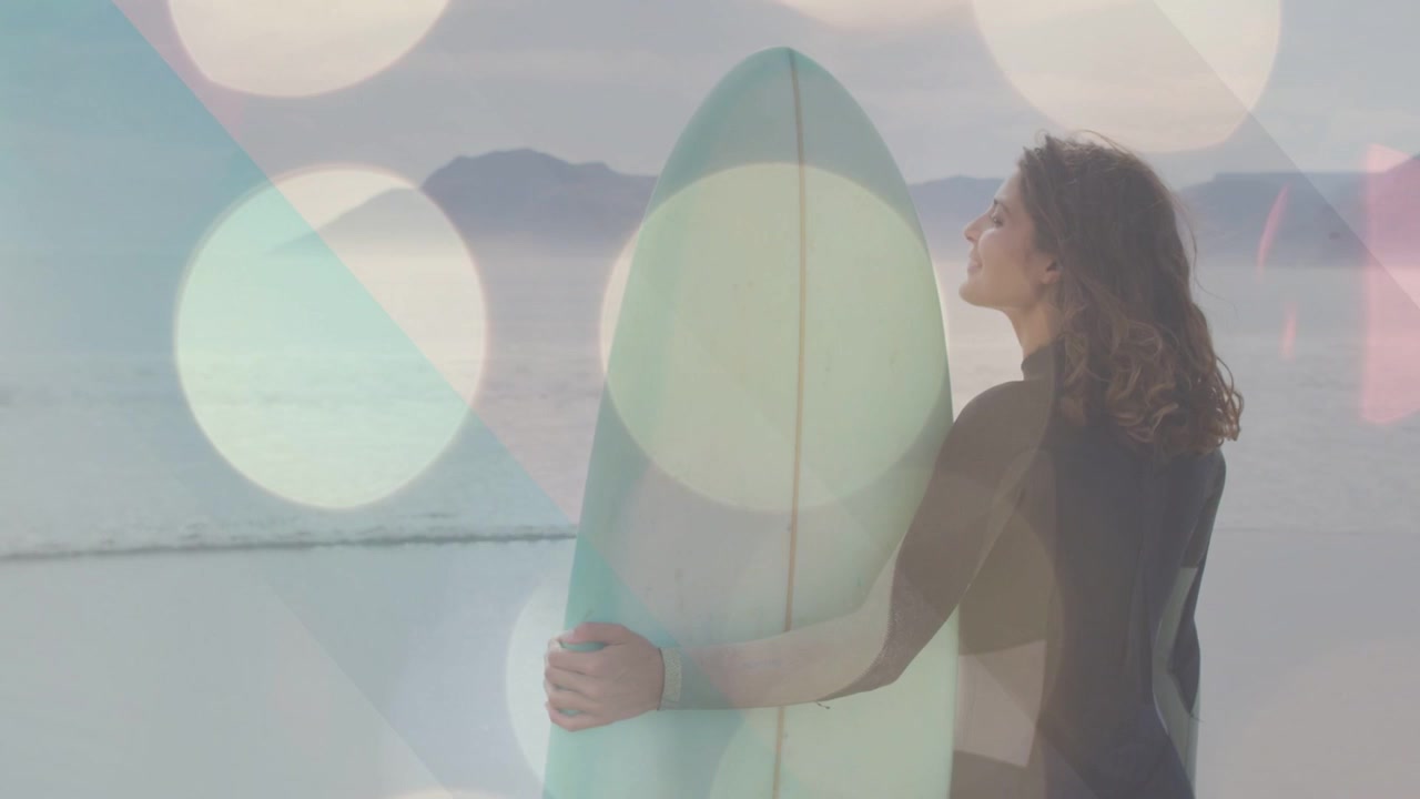 Donna con tavola da surf color menta sulla riva, individua le onde, si gira e si prepara a fare surf, con effetto bokeh sull'inquadratura.