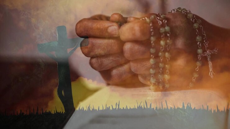 Adult hands praying with rosary over book, fingers sliding beads while crucifix overlay brightening