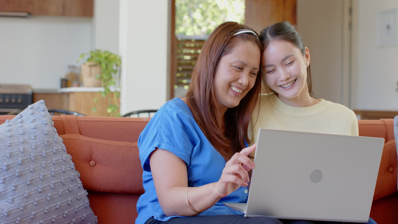 Sitting on couch, asian mother and daughter using laptop, enjoying quality time together