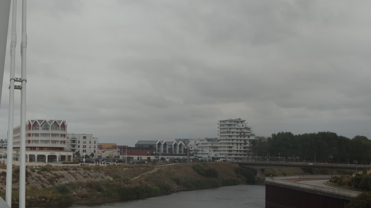 Camera slowly pans across modern bridge, riverfront buildings, and cloudy urban landscape in Dunkirk