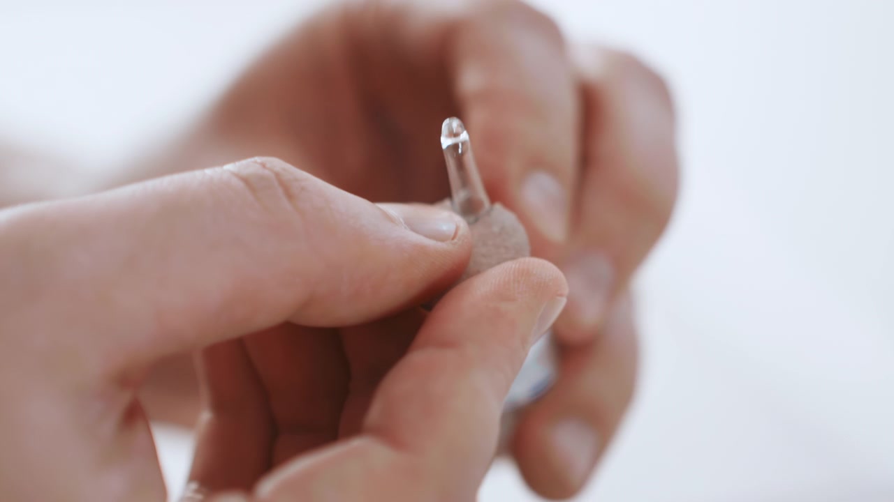 Primer plano de manos ajustando audífono, enfermera negra de atención domiciliaria en una escena doméstica suave mostrando a la cuidadora limpiando el dispositivo, insertando la cúpula de silicona, ajustando el volumen y comprobando el ajuste, toque tierno, luz natural suave