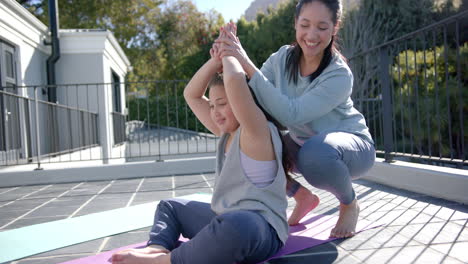 Happy-biracial-mother-and-daughter-practising-yoga-on-terrace-in-sunny-day,-slow-motion