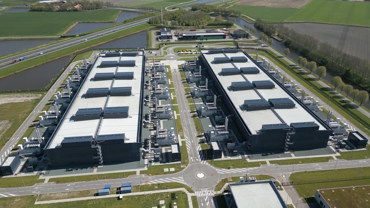 Droneoptagelse fra oven, der viser symmetriske rækker af moderne datacenterbygninger omgivet af kanaler, veje og åbent landbrugsland i Holland