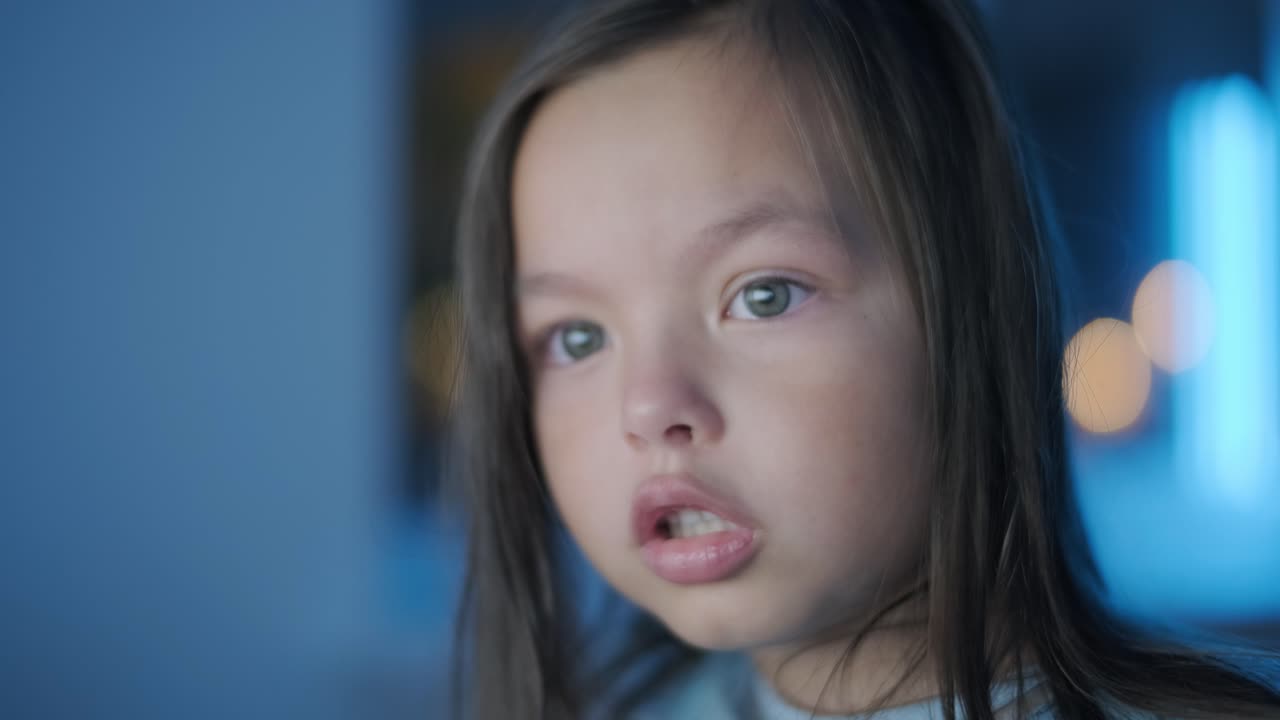 어린 소녀가 컴퓨터 앞에 앉아서 강한 감정을 표시합니다. 이 장면은 편안한 실내 환경에서 펼쳐지는 매력적인 순간 동안 그녀의 표현적 반응을 포착합니다.