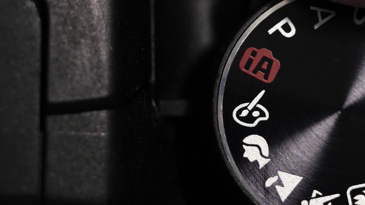 Top down macro of black mode dial rotating on black camera body with white icons