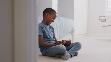 Boy-Sitting-On-Floor-In-Bedroom-Using-Digital-Tablet