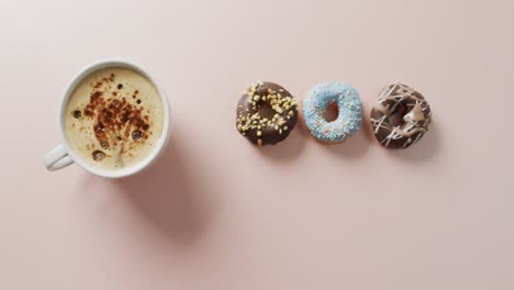 video of donuts with icing and cup of coffee on pink background