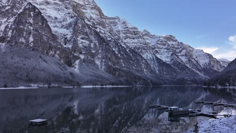 el dron se dirige hacia el pequeño muelle de botes en klöntalersee, glarus, suiza, rodeado de montañas cubiertas de nieve y aguas serenas.