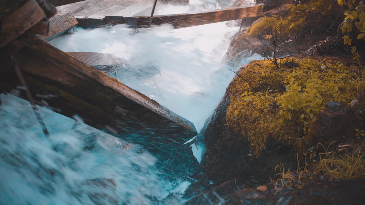 rápidos de agua corriendo a través de la rampa de troncos y chocando contra vigas de madera dañadas de la rampa de troncos cubiertas de musgo mientras rocían niebla y agua sobre rocas cubiertas de musgo durante el otoño 4k prores