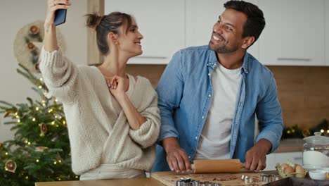 Pareja-Feliz-Teniendo-Videollamada-En-La-Cocina-Mientras-Hornea-Galletas-Navideñas.