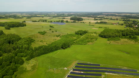 aerial backwards flight over large solar farm complex surrounded by green landscape in nature