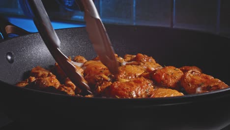 cooking and flipping spicy marinated chicken breast in a pan using tongs