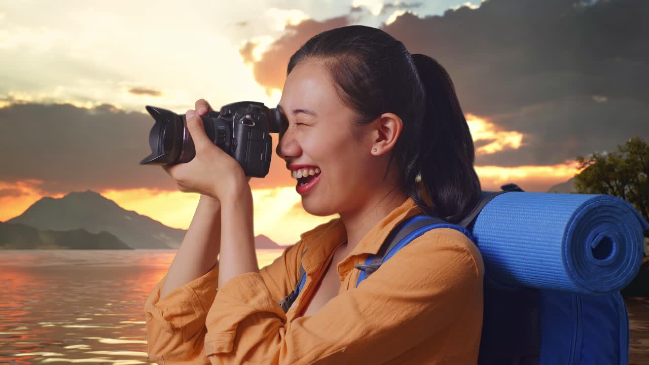 Close Up Side View Of Asian Female Hiker With Mountaineering Backpack Using A Camera Taking Picture While Standing At A Lake During Sunset Time