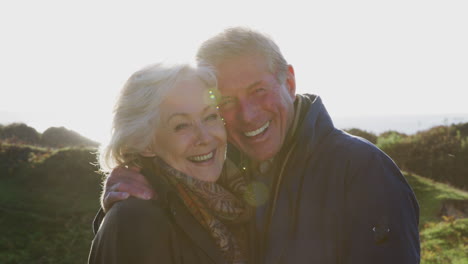 portrait of loving active senior couple walking along coastal path against flaring sun