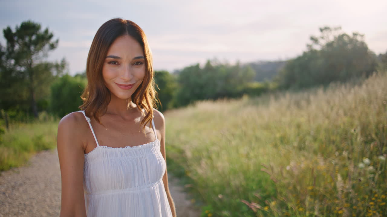 Flirty woman stretching spikelet to camera strolling village path alone portrait