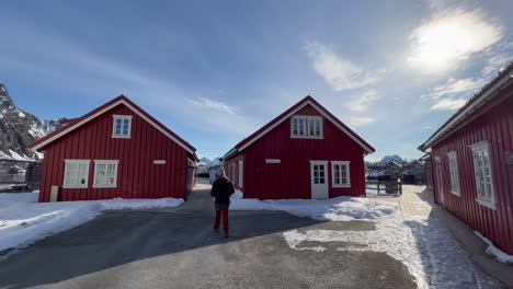 Joven-Turista-Caminando-Hacia-Cabañas-Tradicionales-De-Pescadores-Noruegos-En-Un-Día-Soleado,-Explorando-La-Vista