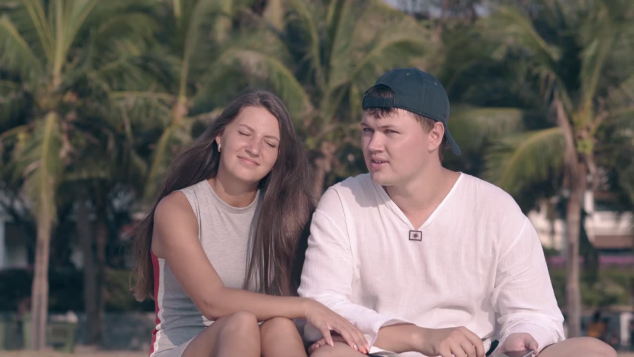 검은 모자를 입은 남자가 회색 드레스를 입은 갈색 여성에게 무언가를 보여줍니다.