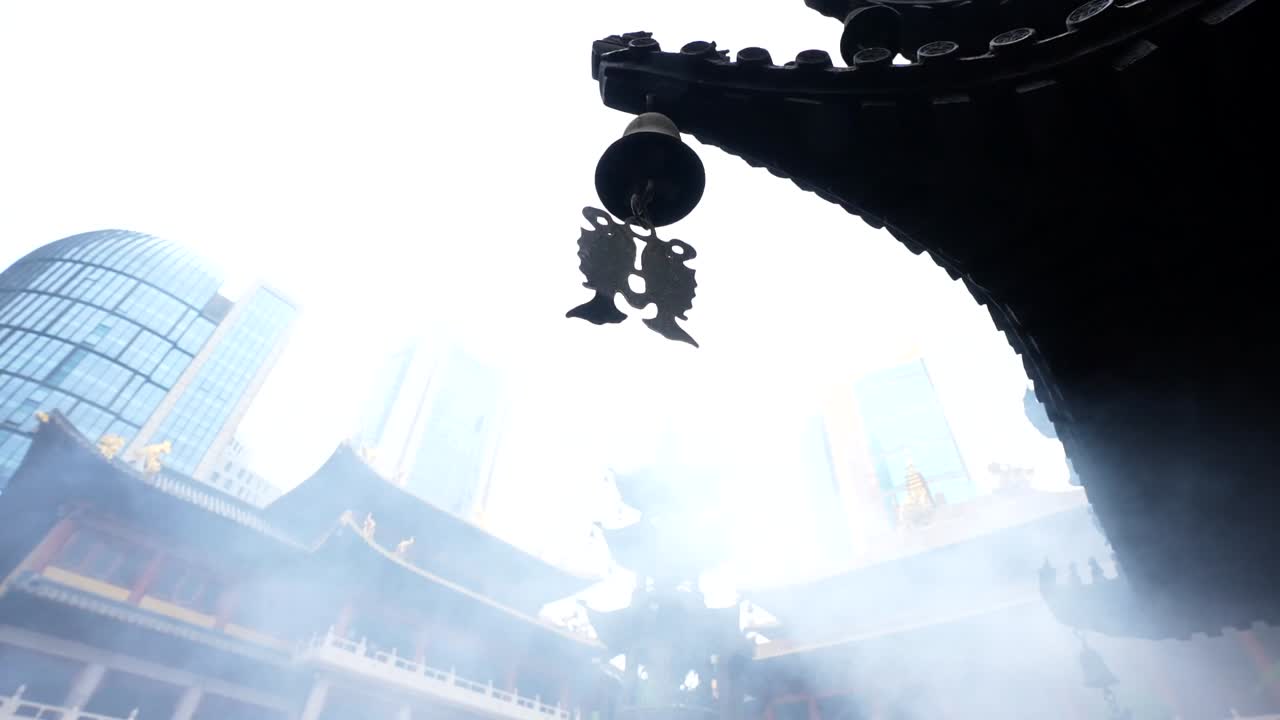 Small bell surrounded by smoke hanging from a corner of a building at Jingan Temple, Shanghai, China