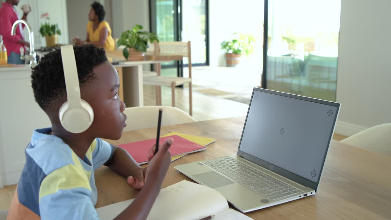 Afroamerikansk familie. Sønnen har høretelefoner på, mens han koncentrerer sig om sin bærbare computer og laver lektier derhjemme.