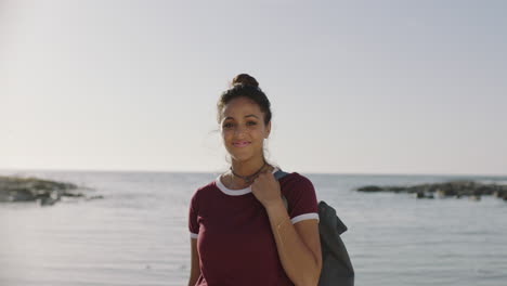 Porträt-Einer-Schönen-Hispanischen-Frau,-Die-Glücklich-Am-Sonnigen-Strand-Lächelt-Und-Einen-Rucksack-Hält