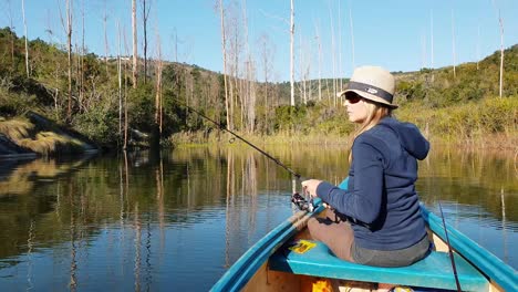 a girl fishing from a canoe on a calm lake next to a beautiful forest