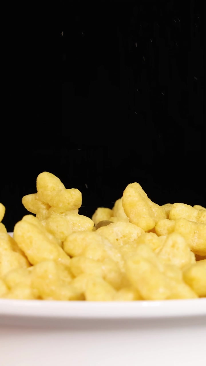 Pezzi di cereali a forma di stella cadono in una ciotola su uno sfondo nero, creando una scena dinamica e giocosa.