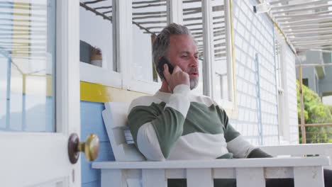 Happy-caucasian-mature-man-siting-on-the-terrace-and-using-smartphone