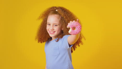 retrato de estudio de una chica comiendo rosquillas contra un fondo amarillo