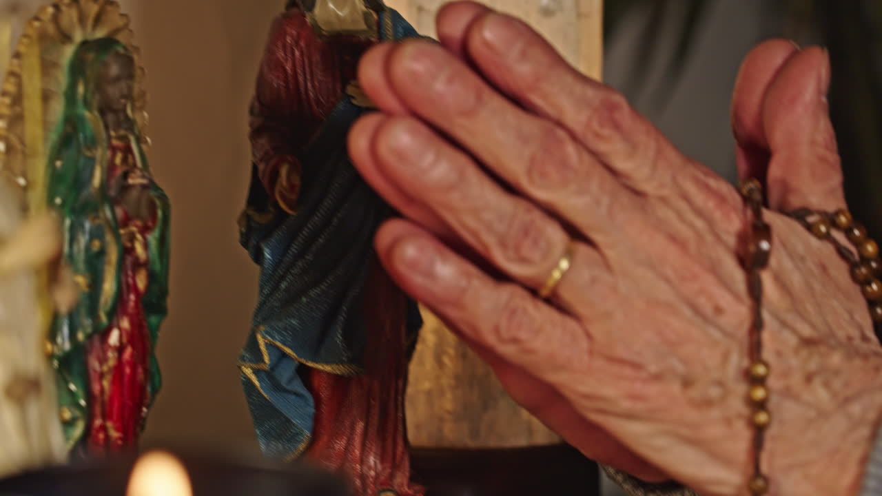Manos de ancianos unidas en oración con rosario y estatuas religiosas