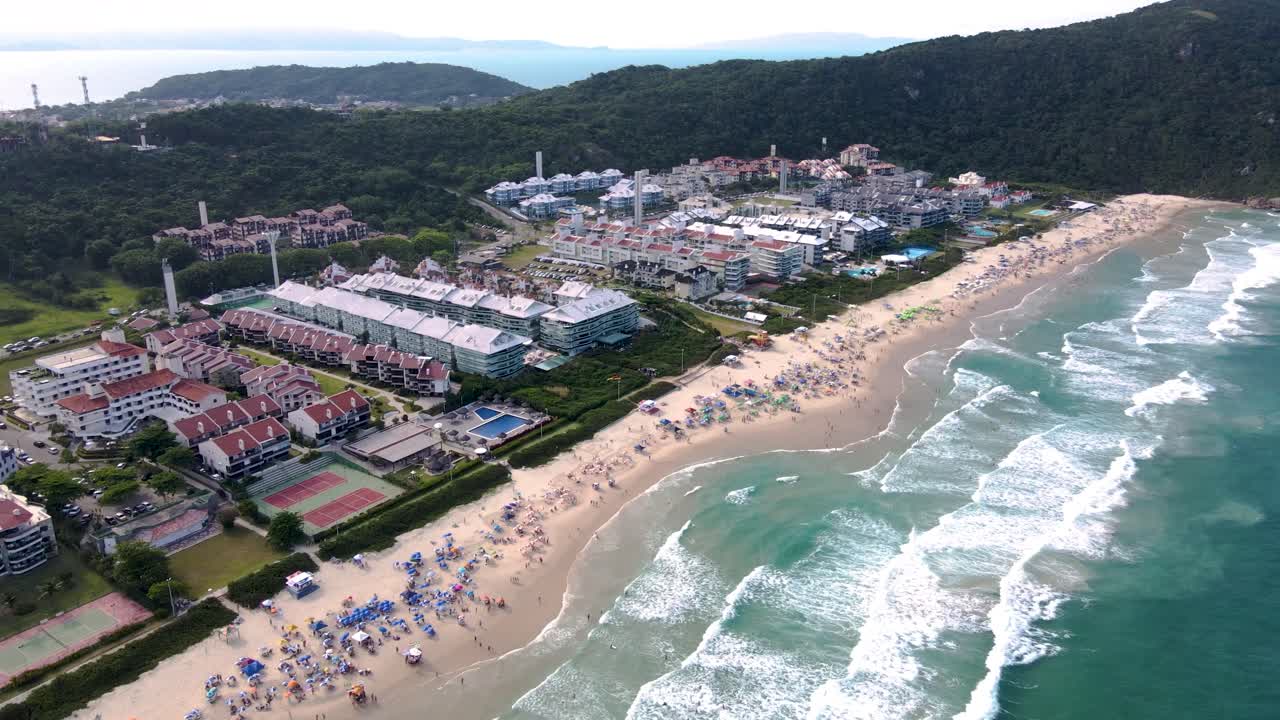 모래 위 에 많은 사람 들 이 있는 바다 를 바라보는 호텔 과 여름집 이 있는 열대 관광 해변 의 공중 풍경