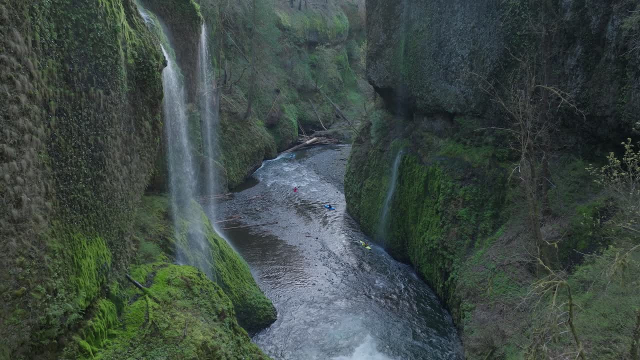 Kayakers navigate underneath waterfalls in a river in the Pacific Northwest.