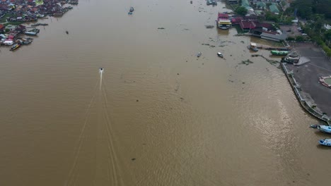motor boat speeding on musi river in city of palembang, aerial drone view