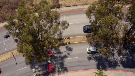 A-curved-road-with-cars-and-surrounding-trees,-casting-shadows,-aerial-view