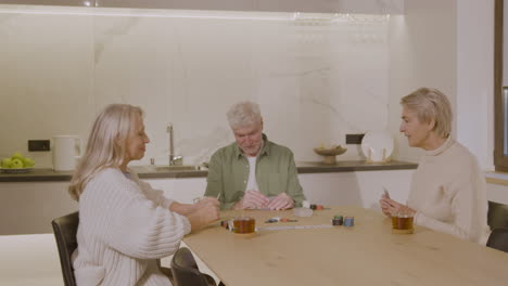 three happy senior friends playing poker at home