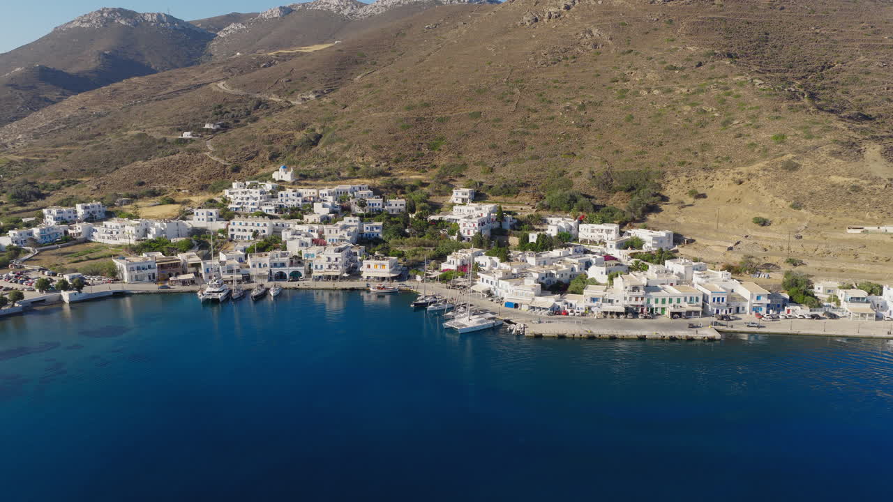 Katapola village by the sea with white houses and dry mountains, Amorgos Island, aerial panoramic drone pullback